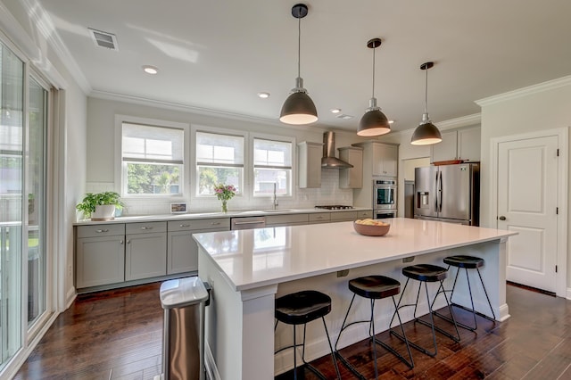 kitchen featuring stainless steel appliances, gray cabinetry, decorative backsplash, crown molding, and wall chimney exhaust hood