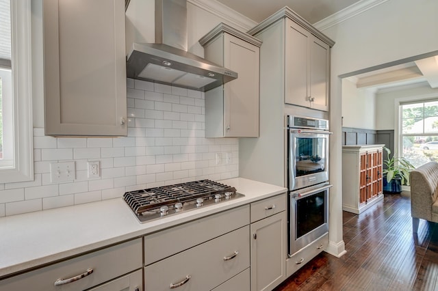 kitchen with wall chimney exhaust hood, appliances with stainless steel finishes, crown molding, gray cabinets, and light countertops
