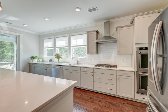 kitchen with wall chimney range hood, stainless steel appliances, a sink, crown molding, and dark wood-type flooring