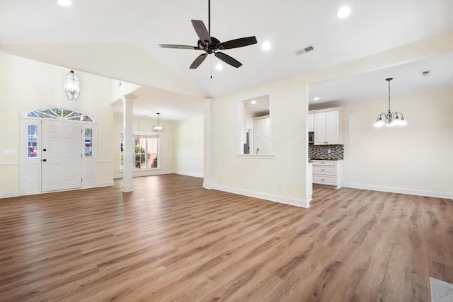 unfurnished living room featuring ceiling fan with notable chandelier, light hardwood / wood-style floors, vaulted ceiling, and ornate columns