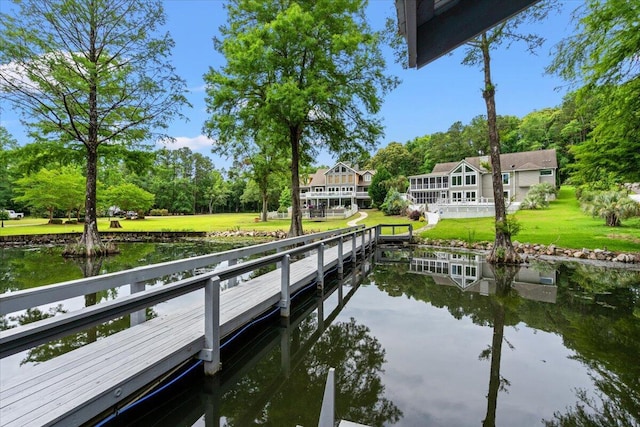dock area featuring a water view, a lawn, and view of wooded area