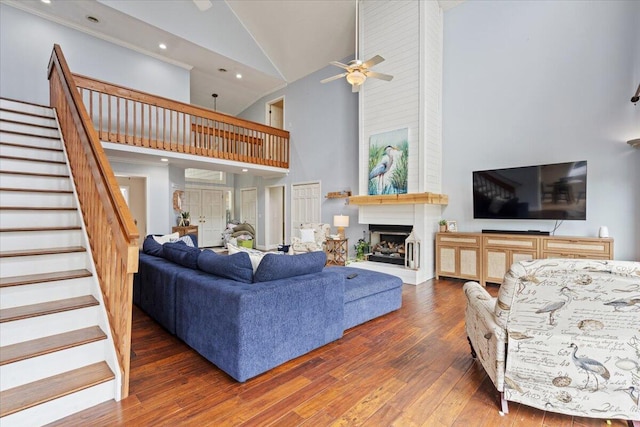 living room with high vaulted ceiling, hardwood / wood-style floors, ceiling fan, stairs, and a fireplace