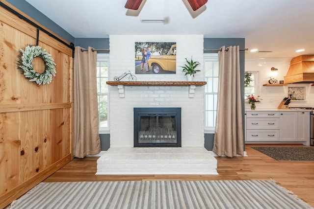 unfurnished living room featuring a barn door, ceiling fan, a fireplace, and light hardwood / wood-style flooring