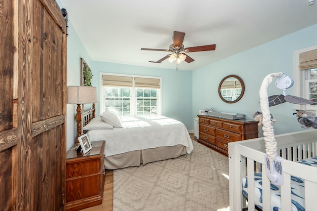 bedroom featuring ceiling fan, a barn door, and light wood-type flooring