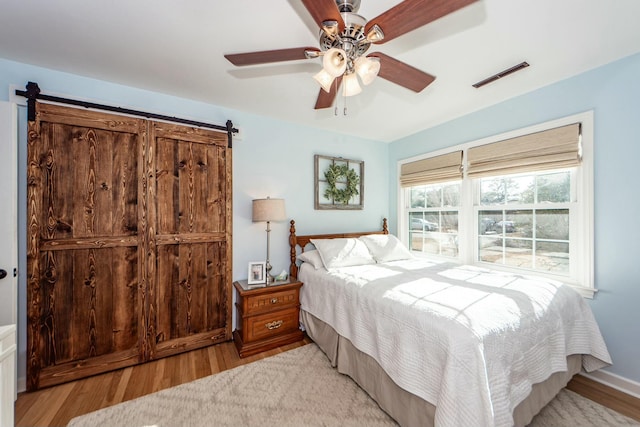 bedroom featuring ceiling fan, a barn door, and light hardwood / wood-style floors