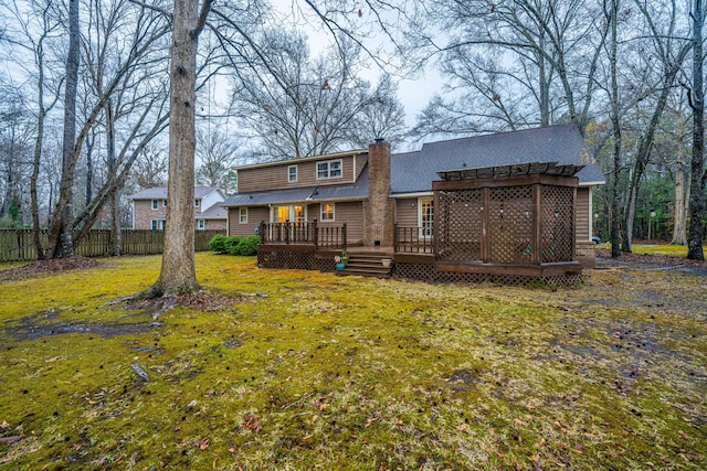 rear view of house featuring a lawn, fence, roof with shingles, a wooden deck, and a chimney