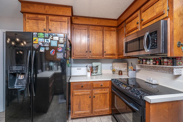 kitchen with black appliances, light countertops, light tile patterned floors, brown cabinetry, and a textured ceiling