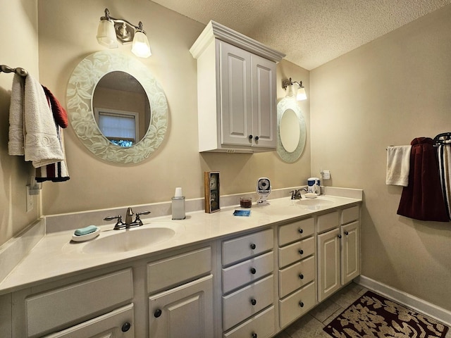 full bathroom with double vanity, a textured ceiling, tile patterned floors, and baseboards