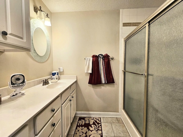 bathroom featuring baseboards, a shower with door, a textured ceiling, vanity, and tile patterned flooring
