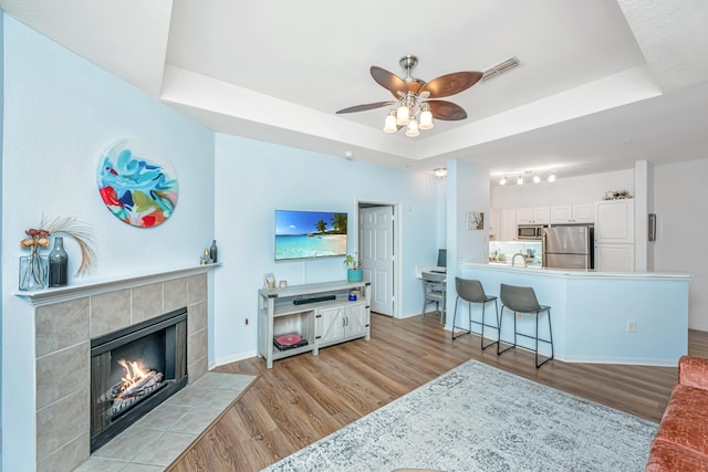 living room featuring a tray ceiling, a fireplace, and light wood-type flooring