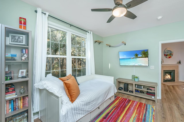 bedroom with ceiling fan, a tiled fireplace, and hardwood / wood-style floors