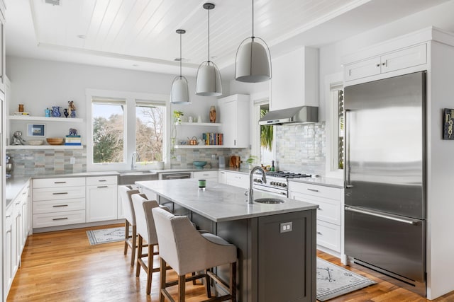 kitchen featuring white cabinetry, wall chimney exhaust hood, an island with sink, and stainless steel built in fridge