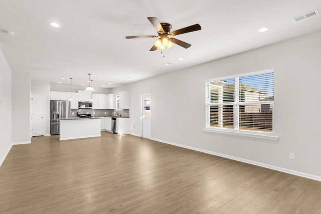 unfurnished living room featuring a wealth of natural light, ceiling fan, and dark hardwood / wood-style floors