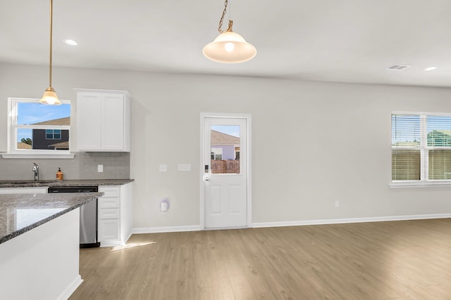 kitchen with white cabinetry, hanging light fixtures, tasteful backsplash, stainless steel dishwasher, and dark stone countertops