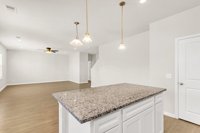 kitchen with light wood-type flooring, ceiling fan, white cabinets, a kitchen island, and hanging light fixtures