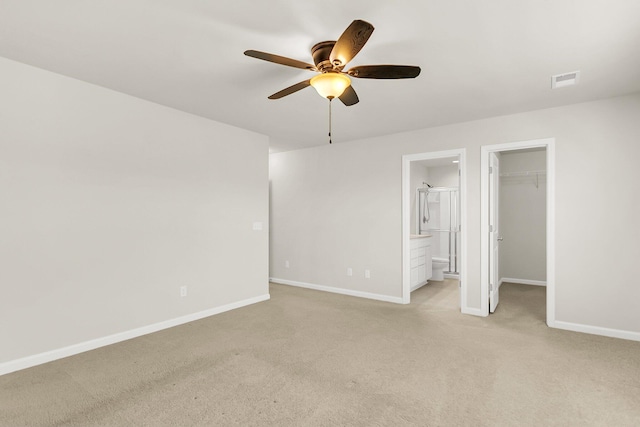 unfurnished bedroom with ceiling fan, light colored carpet, a spacious closet, and connected bathroom