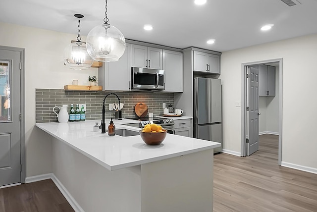 kitchen with pendant lighting, sink, gray cabinetry, stainless steel appliances, and kitchen peninsula