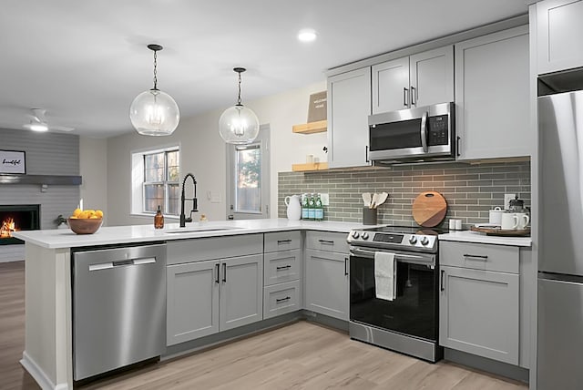 kitchen with sink, gray cabinetry, a large fireplace, kitchen peninsula, and stainless steel appliances