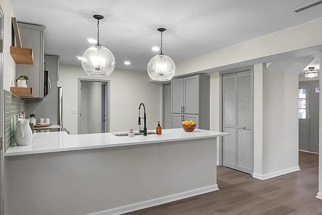 kitchen with gray cabinets, pendant lighting, sink, dark hardwood / wood-style flooring, and kitchen peninsula