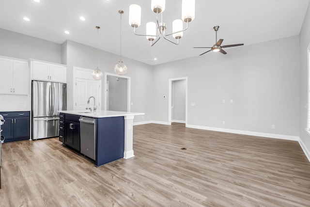 kitchen featuring decorative light fixtures, sink, white cabinets, stainless steel appliances, and a center island with sink