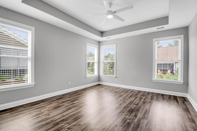 empty room featuring ceiling fan, a tray ceiling, plenty of natural light, and dark wood-type flooring