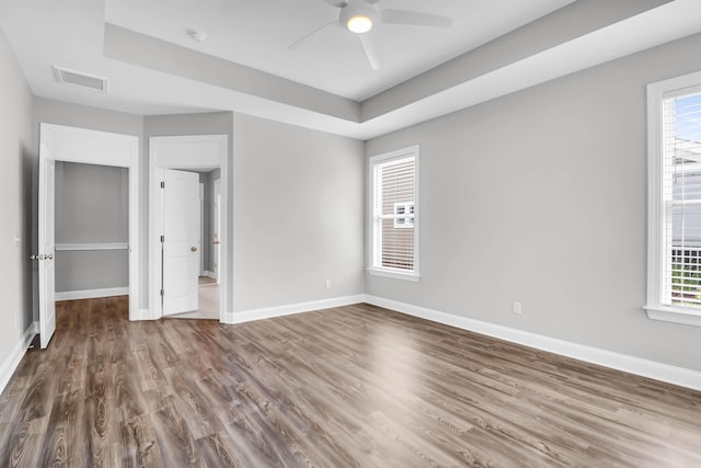 unfurnished bedroom with ceiling fan, wood-type flooring, a tray ceiling, and multiple windows