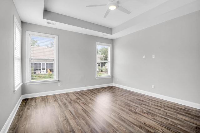 empty room with hardwood / wood-style flooring, ceiling fan, and a tray ceiling