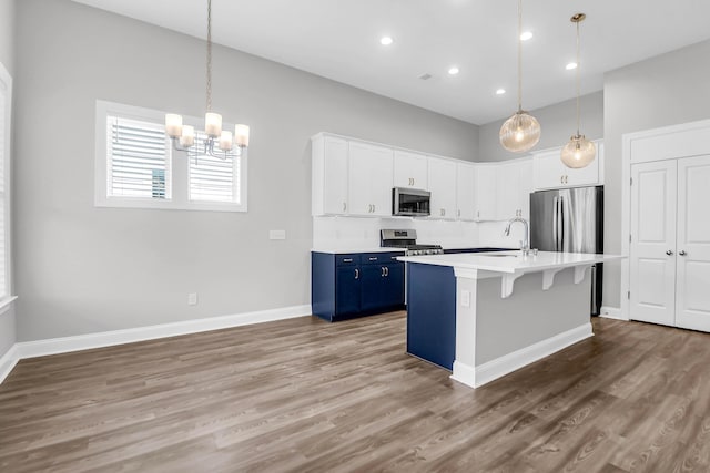 kitchen with stainless steel appliances, white cabinetry, blue cabinetry, and pendant lighting