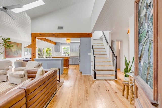 living area featuring a skylight, light wood finished floors, visible vents, high vaulted ceiling, and stairs