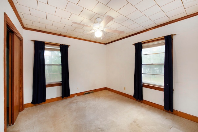 carpeted spare room featuring ceiling fan, ornamental molding, and a healthy amount of sunlight