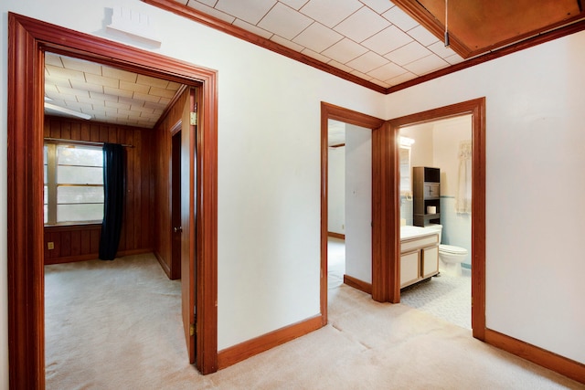 corridor featuring light carpet, wooden walls, and ornamental molding