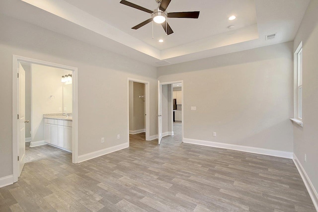 unfurnished bedroom featuring baseboards, visible vents, a tray ceiling, recessed lighting, and light wood-type flooring