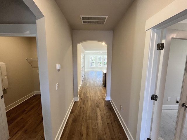 corridor featuring arched walkways, dark wood-style floors, visible vents, and baseboards