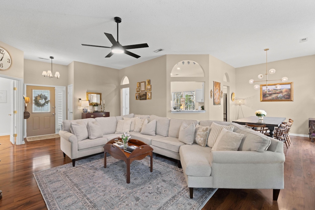 living room featuring dark wood-type flooring and ceiling fan with notable chandelier