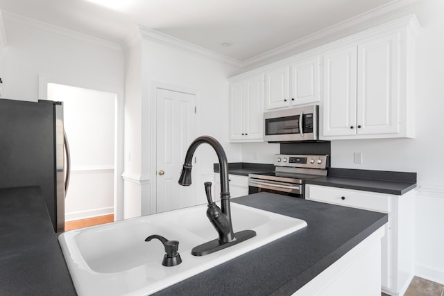 kitchen featuring stainless steel appliances, dark countertops, ornamental molding, white cabinetry, and a sink