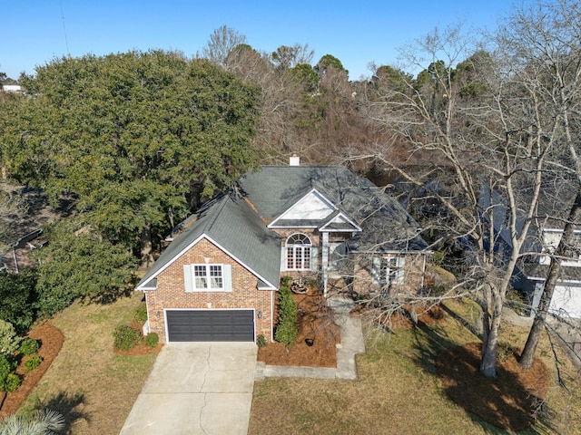 traditional home with brick siding, a chimney, concrete driveway, an attached garage, and a front yard