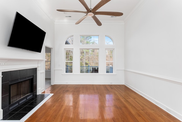 unfurnished living room with crown molding, visible vents, wood finished floors, a tile fireplace, and baseboards