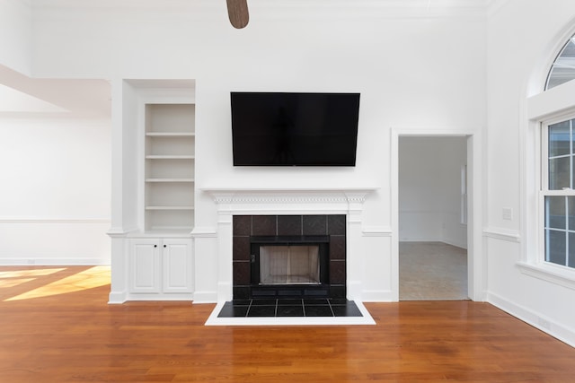 unfurnished living room with wood finished floors, a tile fireplace, and built in features