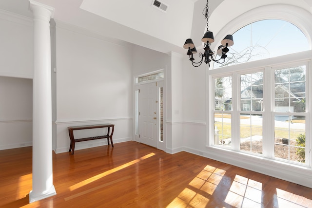 unfurnished dining area with a chandelier, visible vents, ornate columns, and wood finished floors