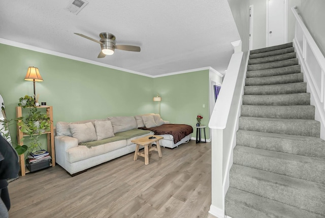 living room featuring crown molding, visible vents, stairway, a ceiling fan, and wood finished floors