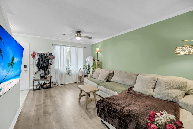 living room with ornamental molding, light wood-type flooring, visible vents, and a ceiling fan