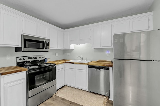 kitchen featuring stainless steel appliances, butcher block countertops, a sink, white cabinets, and light wood finished floors