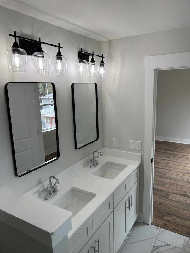 bathroom with double vanity, baseboards, marble finish floor, and a sink