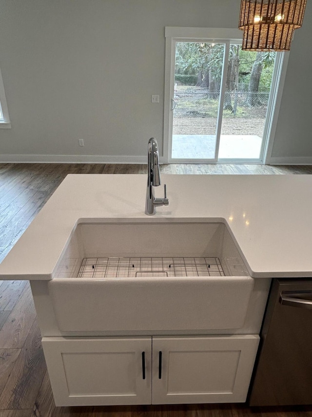 details featuring dark wood-type flooring, a sink, stainless steel dishwasher, white cabinetry, and light countertops