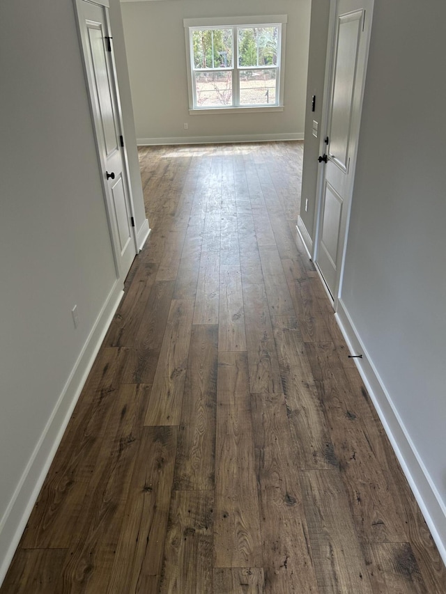 corridor featuring baseboards and dark wood-style flooring