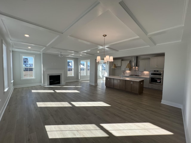 kitchen featuring a healthy amount of sunlight, a kitchen island with sink, wall chimney exhaust hood, and coffered ceiling