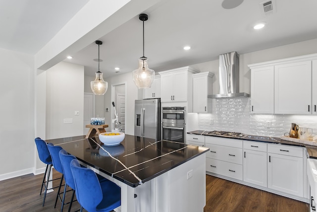 kitchen with a kitchen bar, wall chimney exhaust hood, stainless steel appliances, and white cabinetry