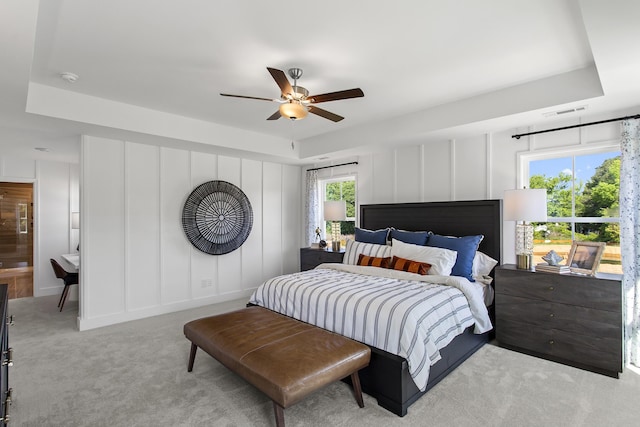 bedroom with light carpet, ceiling fan, a raised ceiling, and ensuite bath