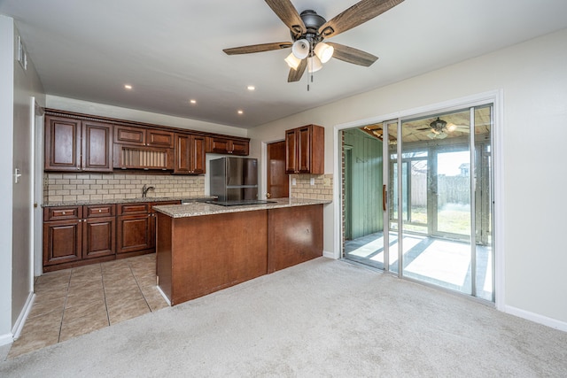 kitchen featuring tasteful backsplash, light colored carpet, freestanding refrigerator, ceiling fan, and light stone countertops