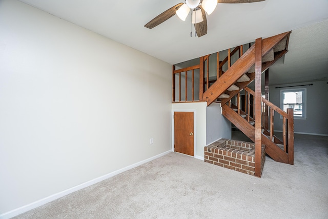 unfurnished living room featuring carpet floors, baseboards, stairway, and a ceiling fan